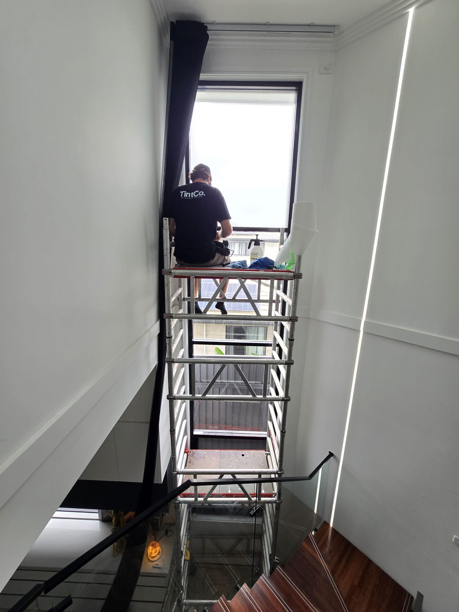 TintCo installer tinting a tall stairwell window